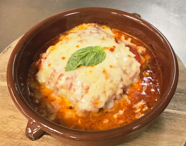 Lasagna in a clay dish with melted mozzarella and basil